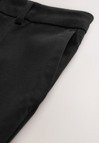 Fekete pamut nadrág sima textúrával, hajtott derékpánttal és finom varrási részletekkel, ferdén elhelyezve.