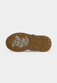 Semelle de chaussure marron avec des crampons profonds et un motif en forme de lézard au centre, vue de dessous sur un fond uni.