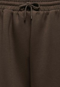 Pantalon de jogging marron en tissu avec taille élastique et cordon noué au centre devant.