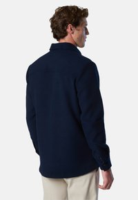 Chemise en laine bleu marine à manches longues, avec des poignets boutonnés et un col pointu. L'arrière présente un détail de basque et un ourlet droit.