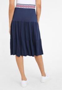 Marineblauwe gelaagde rok met een elastische tailleband, voorzien van een rood en blauw geometrisch patroon, gemaakt van een zachte, rekbare stof.