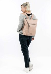 Zaino in pelle rosa chiaro con spallacci regolabili, zip superiore e tasca anteriore. Texture liscia e design minimalista.