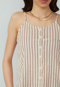 Top met spaghettibandjes in lichtbruin en crèmekleurige verticale strepen, met een knoopsluiting aan de voorkant en een delicate afwerking. Textuurstof.