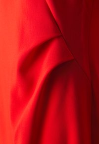 Roter Stoff mit glatter Textur, der weiche Falten aufweist, die dreidimensionale Linien und subtile Kurven erzeugen. Das Design betont einen lebhaften Farbton.