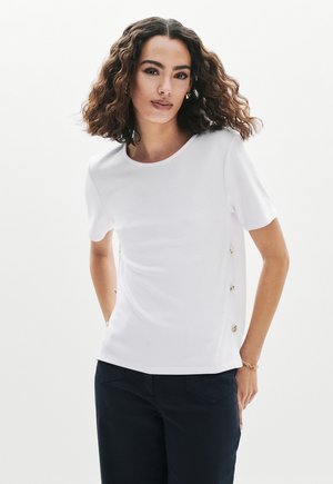 Witte korte mouw top met een ronde halslijn, voorzien van gouden knoopaccenten aan de zijkant, gemaakt van een gladde, lichte stof.