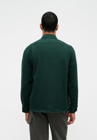 Zielona dzianinowa koszula z kołnierzykiem, długimi rękawami i zapięciem na guziki, posiadająca teksturowany wzór oraz lekko zakrzywiony dół.