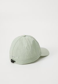 Casquette vert clair en tissu texturé, dotée d'une visière incurvée, d'une sangle d'ajustement à l'arrière et d'une petite étiquette sur le côté.