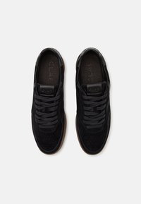 Black suede sneakers with perforated detailing, featuring black laces and a rubber sole. Logo embossed on the tongue. Classic low-top design.