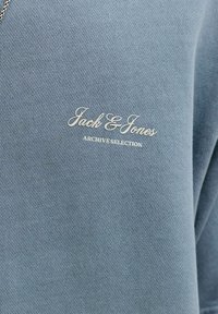 Φωτεινό γαλάζιο πλεκτό ύφασμα με την επιγραφή «Jack & Jones Archive Selection» σε λευκή γραμματοσειρά serif στην περιοχή του στήθους.