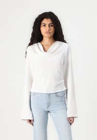 Chemise blanche à col droit à manches longues avec une finition texturée, associée à un jean taille haute bleu clair, présentant une silhouette ajustée.