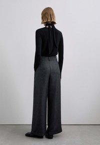 Top negro de manga larga con lazo en la espalda, combinado con pantalones anchos de color gris oscuro. Tela suave, cintura entallada y silueta relajada.