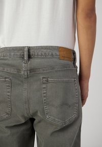 Šedé džíny z denimu s středně vysokým pasem, dvěma zadními kapsami a hnědou koženou nášivkou se značkou "AMERICAN EAGLE" na zadním pase.
