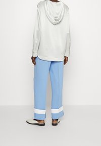 Light gray hooded top, loose blue pants with white cuffs, and cream slip-on shoes. Smooth fabric with a relaxed fit and simple design.