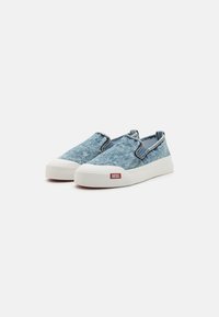 Denim Slipper mit einem hellblauen Stoffoberteil, weißer Gummisohle und kontrastierendem roten logo Aufnäher an der Seite.