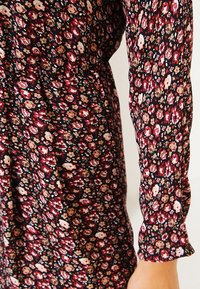 Blommönstrad klänning med en mörk bakgrund och små rosa, röda och vita blommor. Långa ärmar med indragna manschetter, lättviktigt tyg.