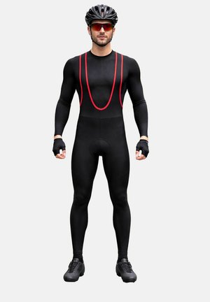 Männlicher Radfahrer, der einen schwarz-roten Rennanzug, einen schwarzen Helm, rot getönte Sonnenbrillen, fingerlose Handschuhe und schwarze Fahrradschuhe trägt und aufrecht steht.