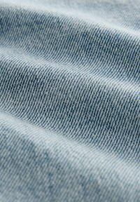 Tejido de mezclilla azul claro con textura de costura diagonal; superficie suave con sutiles variaciones de color y sombreado en toda la tela.