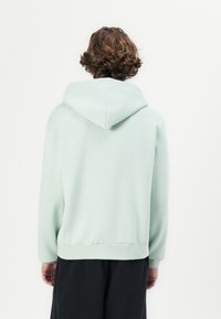 Light green hoodie made of soft fabric, featuring a drawstring hood, ribbed cuffs, and waistband, with a relaxed fit and minimal design.