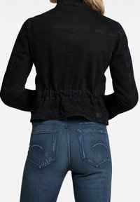 Musta farkkutakki, jossa on istuva malli ja rypytetty vyötärö. Yhdistetty sinisiin farkkuihin, joissa on haalistuneet yksityiskohdat ja takataskut, joissa on kaartuvat ompeleet.