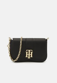 Sac à main noir avec une bandoulière chaîne dorée, un design élégant, une surface texturée et un logo doré proéminent sur le devant.