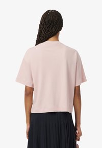 Camiseta recortada de manga corta hecha de suave algodón rosa, con un escote redondo y un corte relajado, vista desde atrás.