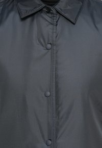 Σκούρο γκρι, ελαφρύ μπουφάν με γυαλιστερή επιφάνεια, που διαθέτει μυτερό γιακά και έξι κουμπιά snap κατά μήκος του μπροστινού μέρους. Μοναδική λεία υφή.