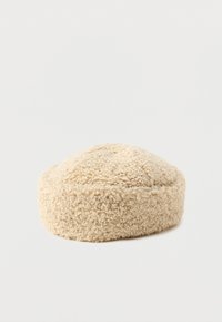 Beige runder Hut aus strukturiertem, flauschigem Material. Er hat eine glatte, leicht erhöhte Oberseite mit einer dezenten Naht um den Boden.