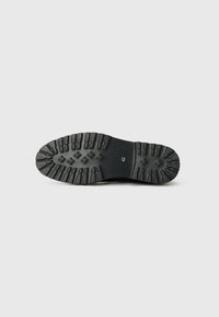 Suela de bota de goma negra con surcos profundos para tracción, que presenta patrones elevados y una marca de talla 42 cerca del talón. Textura suave.