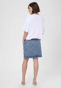 White oversized t-shirt paired with a denim skirt featuring diamond quilted texture and side button details, worn with strappy heels.