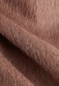 Tejido de textura suave en un tono rosa apagado, con una superficie borrosa y ligeramente peluda. El material parece cálido y acogedor.