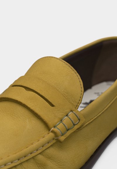 Mocassin en cuir jaune avec couture mocassin et détail de bride fendue sur le dessus, laissant apparaître une partie de la doublure intérieure sombre et de la semelle.