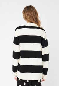 Black and white striped long-sleeve top with a collar, made of soft fabric, featuring wide horizontal stripes and a relaxed fit.