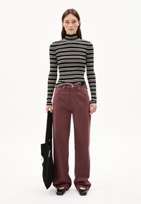 Schwarz-weißer gestreifter Rollkragenpullover, figurbetonte Silhouette. Burgunderfarbene High-Waist-Hose, weit geschnittenes Design. Schwarze Flachschuhe, schwarze Tote-Tasche.