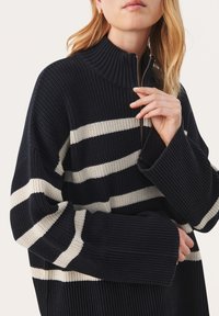Sweter w navy i kremowe paski z wysokim kołnierzem, zamkiem błyskawicznym oraz szerokimi rękawami z prążkowanymi mankietami i teksturowanym materiałem.