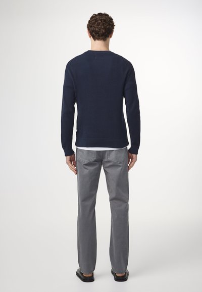 Maglione a coste navy, maniche lunghe, collo a giro. Abbinato a pantaloni grigi a gamba dritta, indossato con sandali neri flat. Sfondo neutro.
