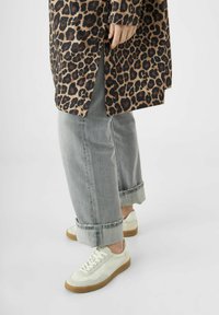Luipaardprint lange shirt, lichtgrijze opgerolde spijkerbroek en witte sneakers met bruine zolen. Materialen en patronen zijn opvallende kenmerken.