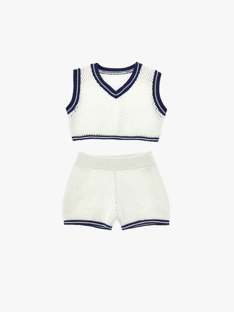 Bijela pletača s kratkim hlačama koja se sastoji od v-izreza, mornarsko plave obrube i teksturiranog tkanja. Tkanina je mekana i ima otvoreni uzorak.