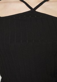 Top de tecido canelado preto com alças cruzadas finas, com um formato ajustado que enfatiza linhas verticais e texturas.