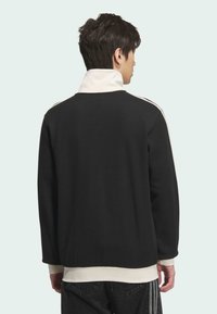 Crni rebrasti pulover s visokim bijelim ovratnikom, dugim rukavima i suptilnim bijelim prugama preko ramena. Mekana tekstura, opušteni kroj.