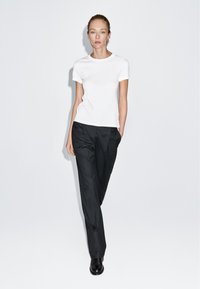 Bílé tričko s krátkým rukávem v kombinaci s černými tailored kalhotami a černými botami. Elegantní, minimalistický design s přiléhavým střihem.