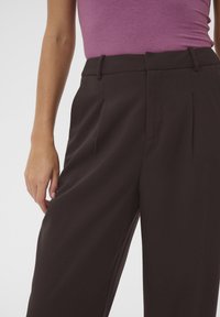 High-waisted, wide-leg trousers in dark brown fabric. Features pleats at the front and belt loops, smooth texture with a clean finish.