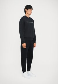 Marineblauwe sweatshirt met het "ARMANI EXCHANGE" logo, gecombineerd met bijpassende marineblauwe joggers en witte sneakers, met een ontspannen pasvorm en geribde manchetten.