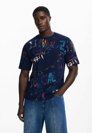 Marinblå t-shirt i bomull med flerfärgade abstrakta grafiska tryck. Kortsleeve och rundad halsringning. Tillsammans med blå denimjeans.