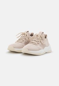 Zapatillas de punto de color beige claro con parte superior texturizada, punta redonda y suela de goma blanca, con cordones a tono y un tirador en el talón.