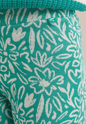 Tyrkysové legíny s vzorom a bielym kvetinovým dizajnom, vyrobené z textúrovaného materiálu. Obsahujú malú značkovú etiketu na páse.