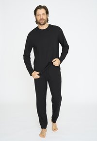 Sort langærmet top og matchende bukser lavet af blødt stof; toppen har en rund halsudskæring, og bukserne har en elastisk linning.