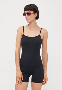 Black sleeveless bodysuit with a fitted design and short legs. Worn with red sunglasses, showcasing a smooth texture and minimal seams.