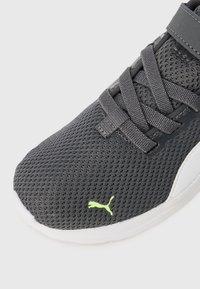 Chaussure de sport en maille grise avec un col rembourré, des lacets plats et un logo noir réfléchissant. Elle dispose d'une semelle en caoutchouc blanche et d'une surface texturée.