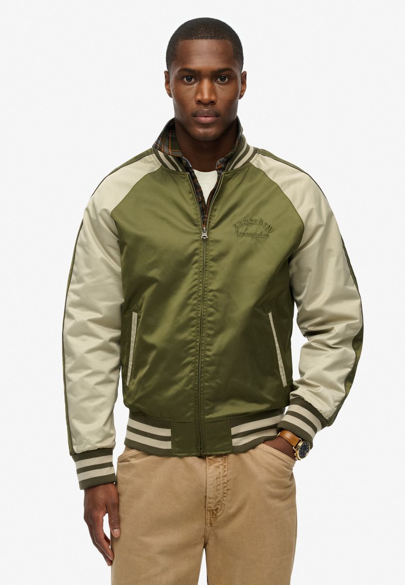 Olivengrøn bomberjakke med beige ærmer, ribbede manchetter og kant. Har broderi, lynlås og plaid-foring. Poly-satin materiale.