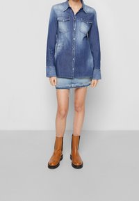 Denimová košilová šaty, odstín od světle modré po tmavě modrou, dvě náprsní kapsy, zapínání na knoflíky, mírně oversize střih, doplněné denimovou minisukní a hnědými kotníkovými botami.